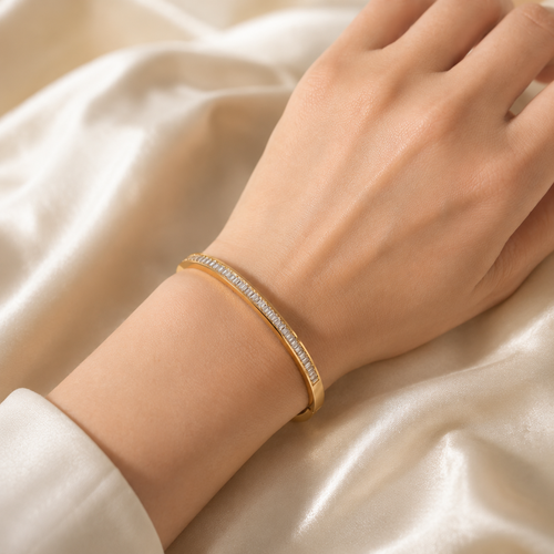 A gold-plated hinged bangle for women featuring a continuous row of channel-set baguette crystals with a secure side-clasp, shown on a model