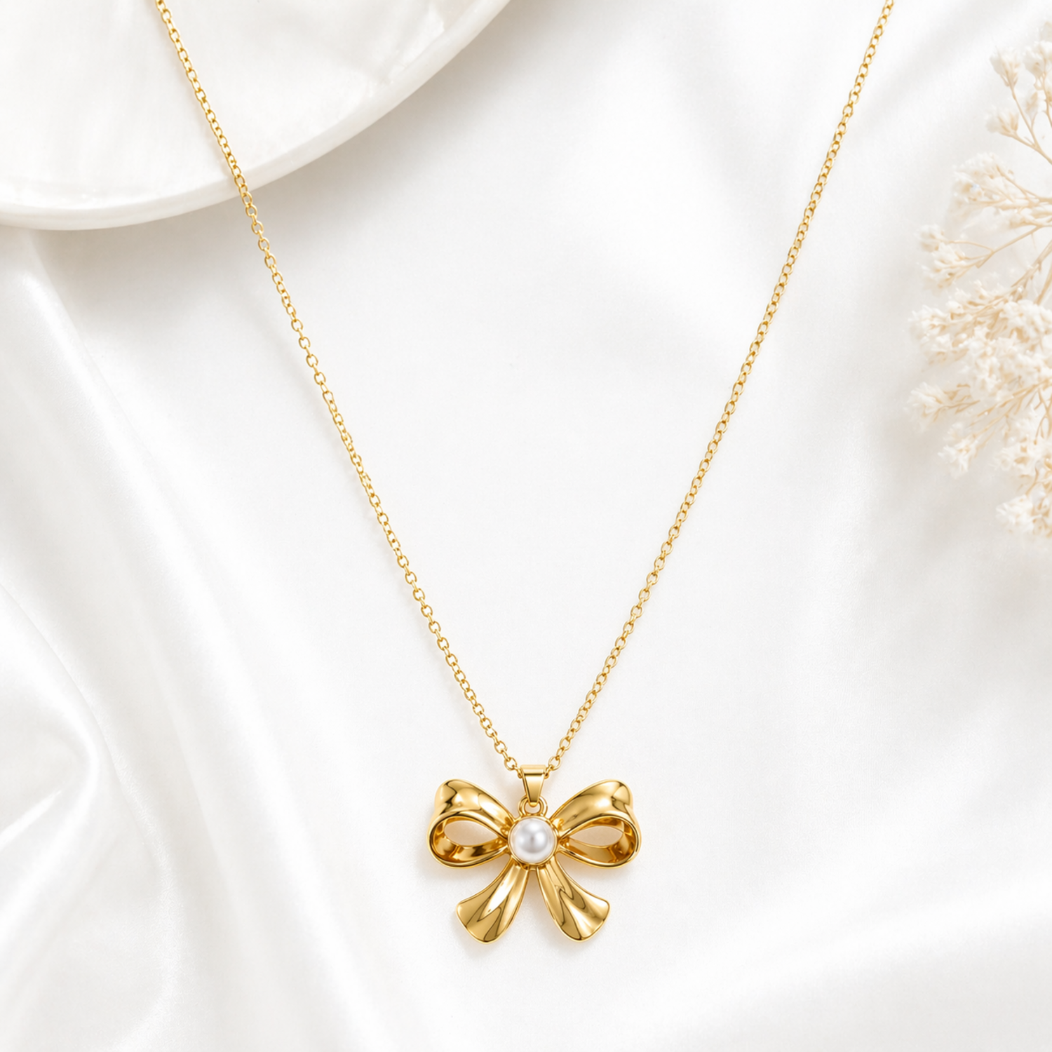 A gold-plated stainless steel chain for women featuring a golden bow pendant with a central pearl, displayed on a white background.