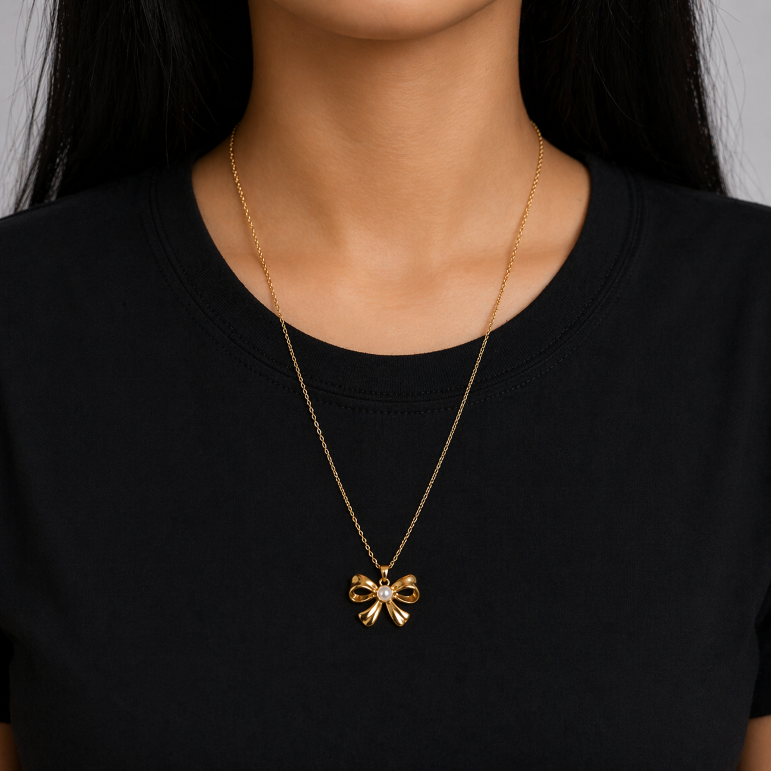 A gold-plated stainless steel chain for women featuring a golden bow pendant with a central pearl, shown on a model