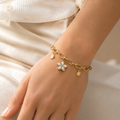 A close-view of a  gold-plated chain bracelet for women featuring a central mother-of-pearl flower charm and two polished star charms on a thick oval-link chain.