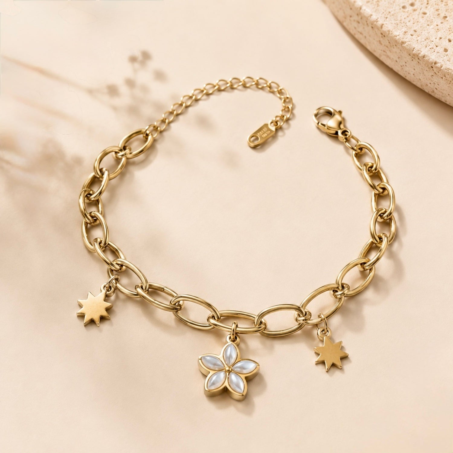 A gold-plated chain bracelet for women featuring a central mother-of-pearl flower charm and two polished star charms on a thick oval-link chain.