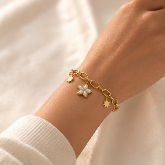 A gold-plated chain bracelet for women featuring a central mother-of-pearl flower charm and two polished star charms on a thick oval-link chain, shown on a model