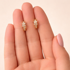 A pair of gold-plated huggie hoop earrings for women featuring a small clear crystal flower design, shown held in a hand.