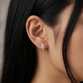 A gold-plated huggie hoop earrings for women featuring a small clear crystal flower design, on a model