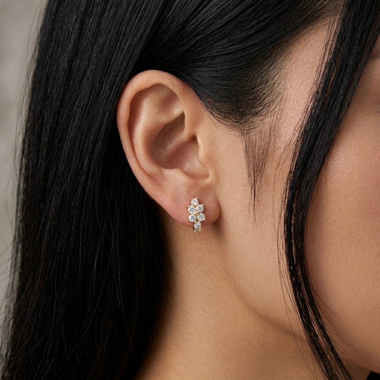 A gold-plated huggie hoop earrings for women featuring a small clear crystal flower design, on a model
