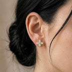 A gold-plated floral stud earrings for women featuring pear-shaped clear crystals in a clover design, shown on a model