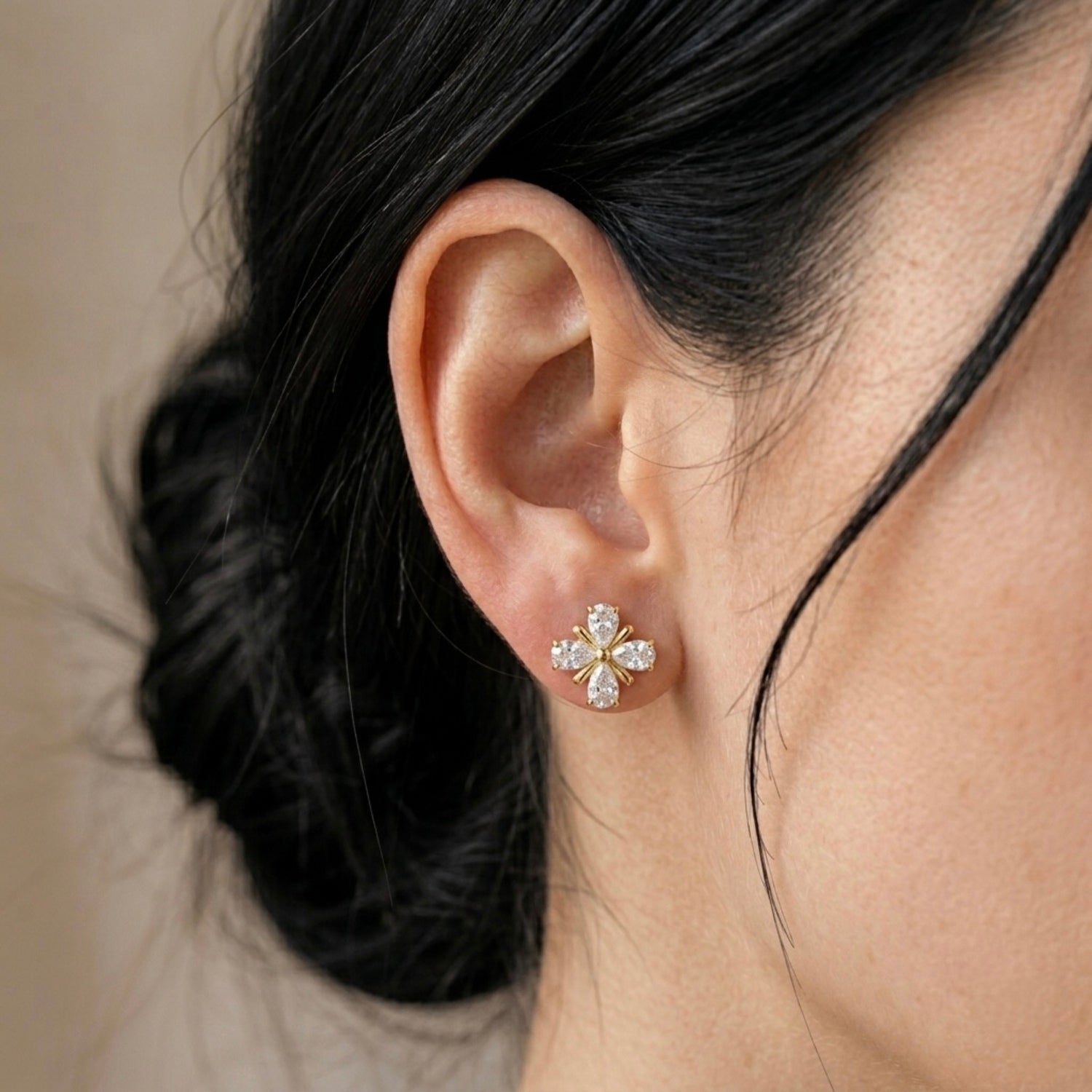A gold-plated floral stud earrings for women featuring pear-shaped clear crystals in a clover design, shown on a model