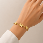A gold-plated cuff bangle for women featuring three frosted-finish butterfly charms and polished circular links, shown on a model hand