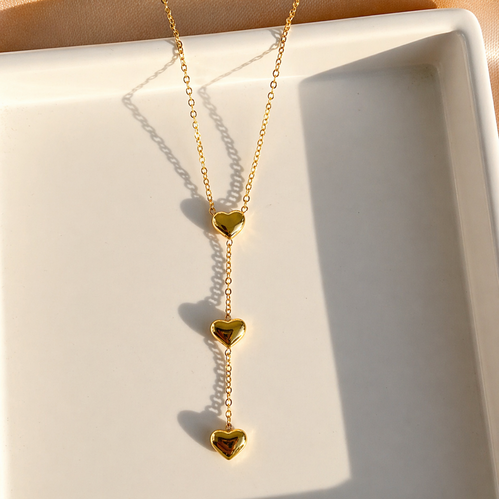 A close-view of a gold-plated stainless steel chain for women featuring a cascading vertical drop of three polished heart pendants