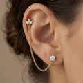 A gold-plated ear chain earrings for women featuring a marquise-cut floral stud and a round white stone stud connected by a delicate gold chain on a model