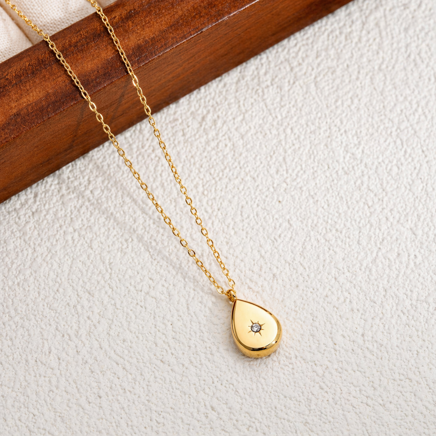 A gold-plated stainless steel chain for women featuring a polished teardrop pendant with a small sparkling crystal set in a starburst engraving