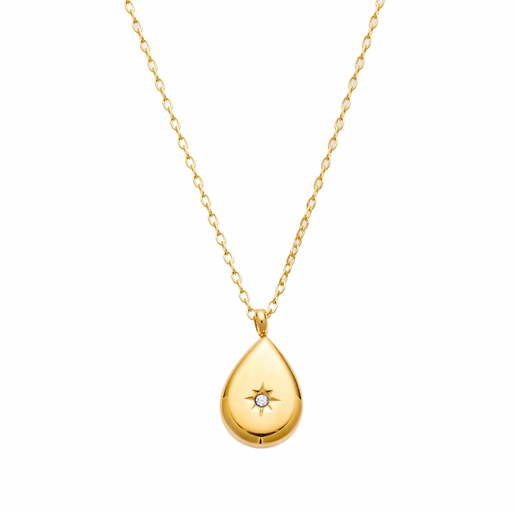 A close-view of a gold-plated stainless steel chain for women featuring a polished teardrop pendant with a small sparkling crystal set in a starburst engraving