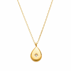 A close-view of a gold-plated stainless steel chain for women featuring a polished teardrop pendant with a small sparkling crystal set in a starburst engraving