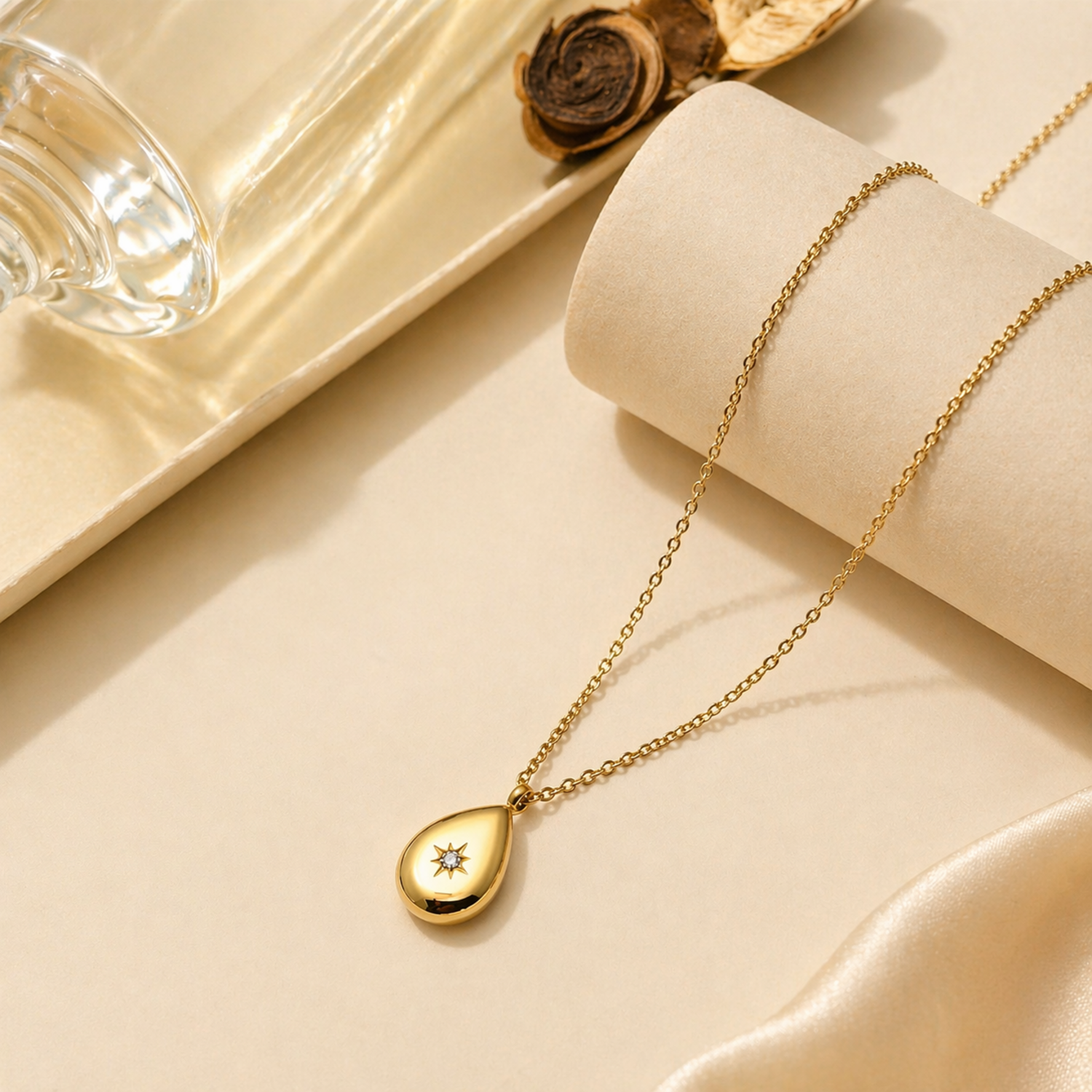 A gold-plated stainless steel chain for women featuring a polished teardrop pendant with a small sparkling crystal set in a starburst engraving