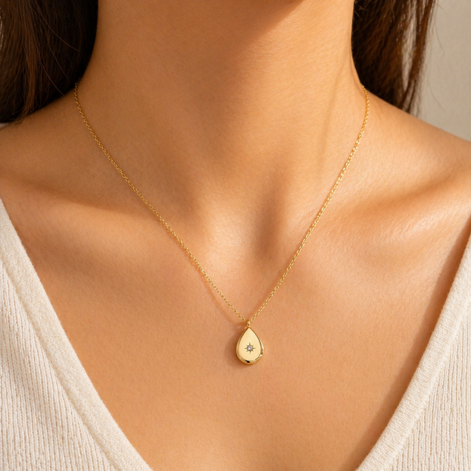 A gold-plated stainless steel chain for women featuring a polished teardrop pendant with a small sparkling crystal set in a starburst engraving shown on a model