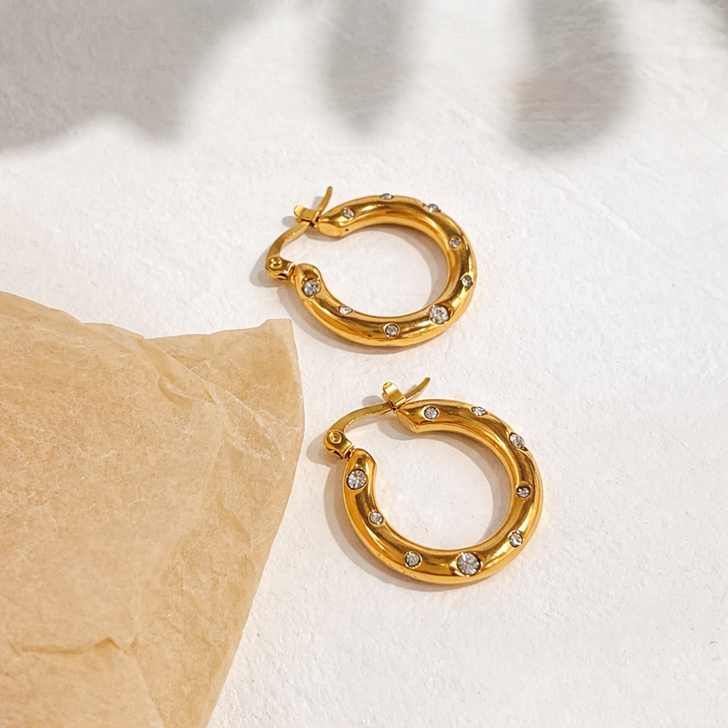 A pair of gold-plated thick hoop earrings for women featuring scattered clear crystals, shown on a white background
