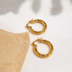 A pair of gold-plated thick hoop earrings for women featuring scattered clear crystals, shown on a white background