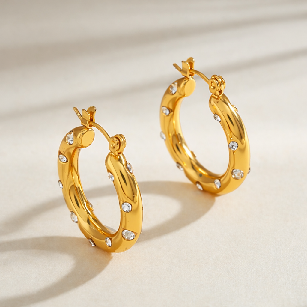 A side-view of a pair of gold-plated thick hoop earrings for women featuring scattered clear crystals, shown on a white background