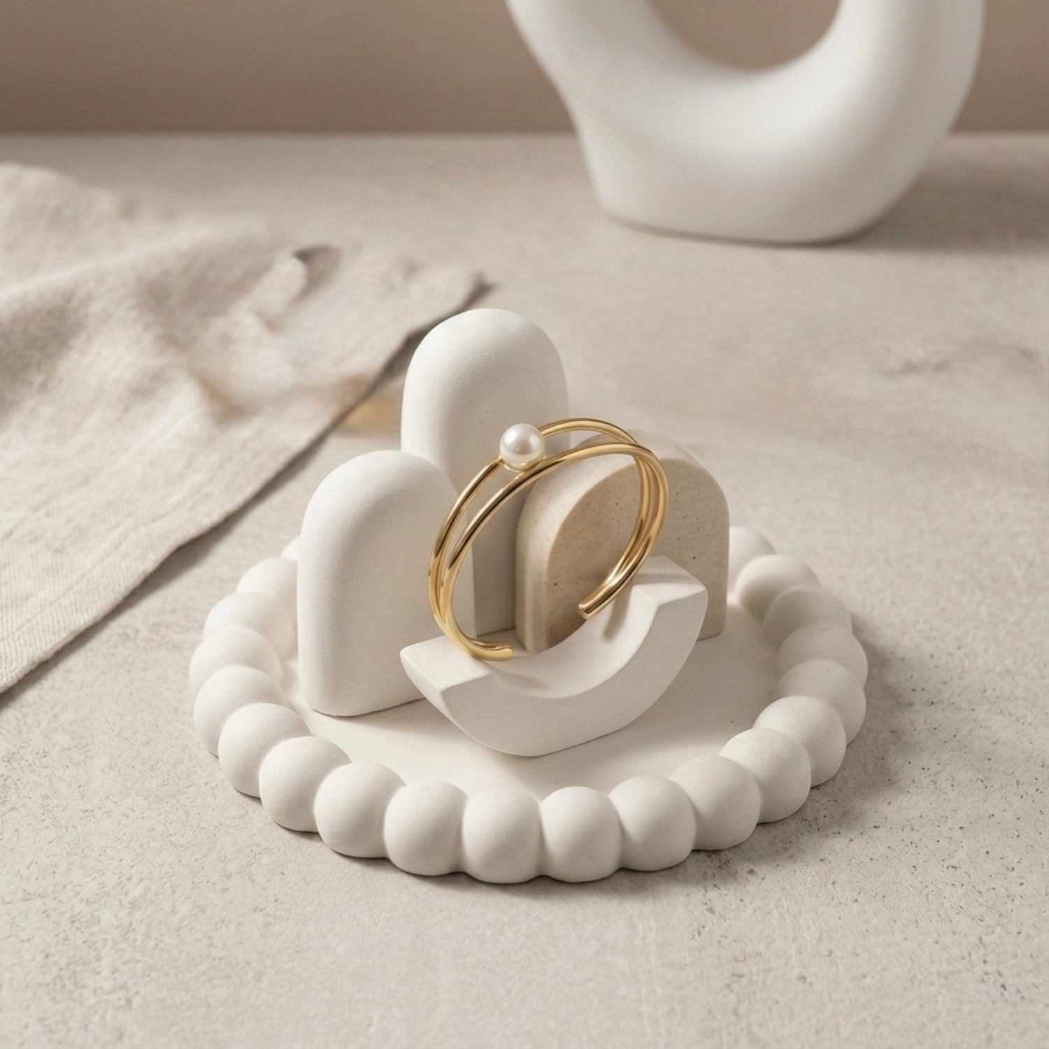 Modern gold-plated double-band adjustable cuff bracelet for women featuring a single central pearl, resting on a white bobbled jewelry dish