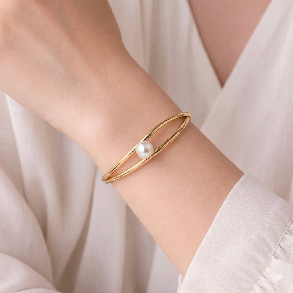 Modern gold-plated double-band adjustable cuff bracelet for women featuring a single central pearl on a model hand
