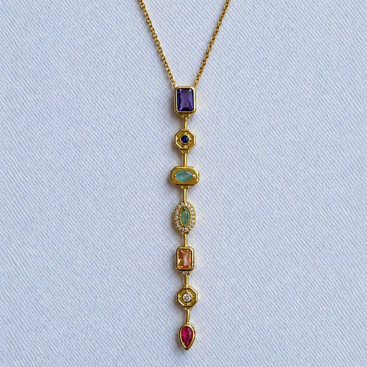 A close-view of a gold-plated stainless steel chain for women featuring a vertical lariat pendant set with various colorful geometric stones