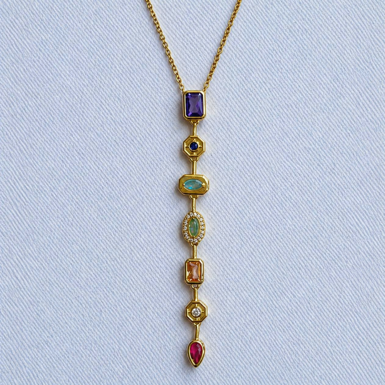 A close-view of a gold-plated stainless steel chain for women featuring a vertical lariat pendant set with various colorful geometric stones