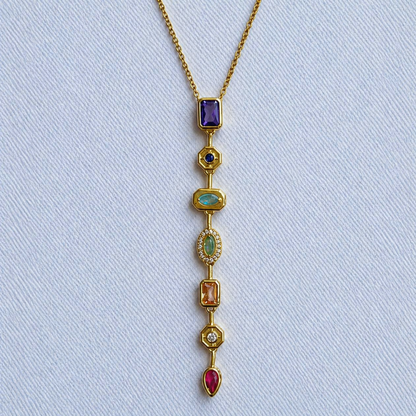 A close-view of a gold-plated stainless steel chain for women featuring a vertical lariat pendant set with various colorful geometric stones