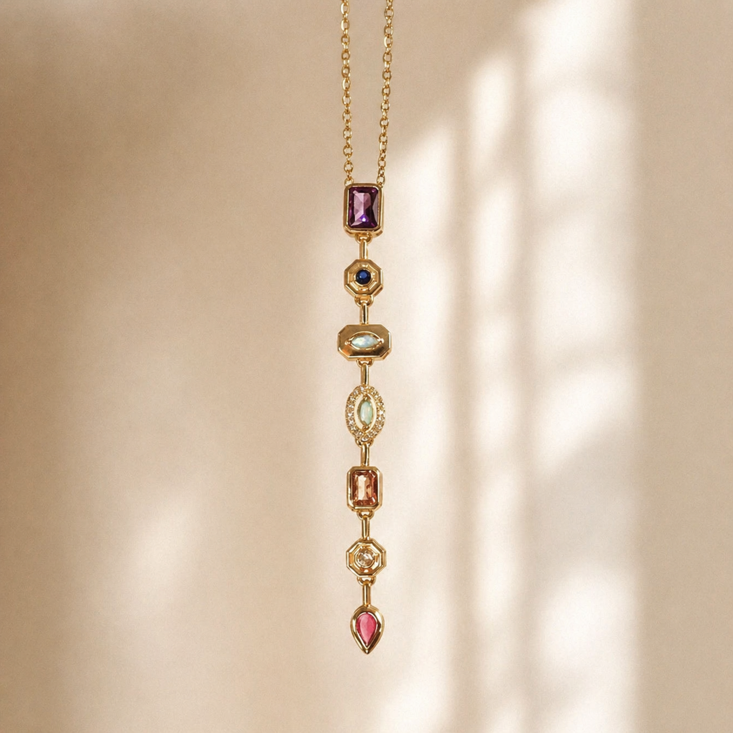 A gold-plated stainless steel chain for women featuring a vertical lariat pendant set with various colorful geometric stones