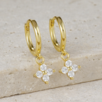 A pair of gold-plated hoop earrings for women featuring a sparkling four-petal crystal clover drop, shown on a textured surface