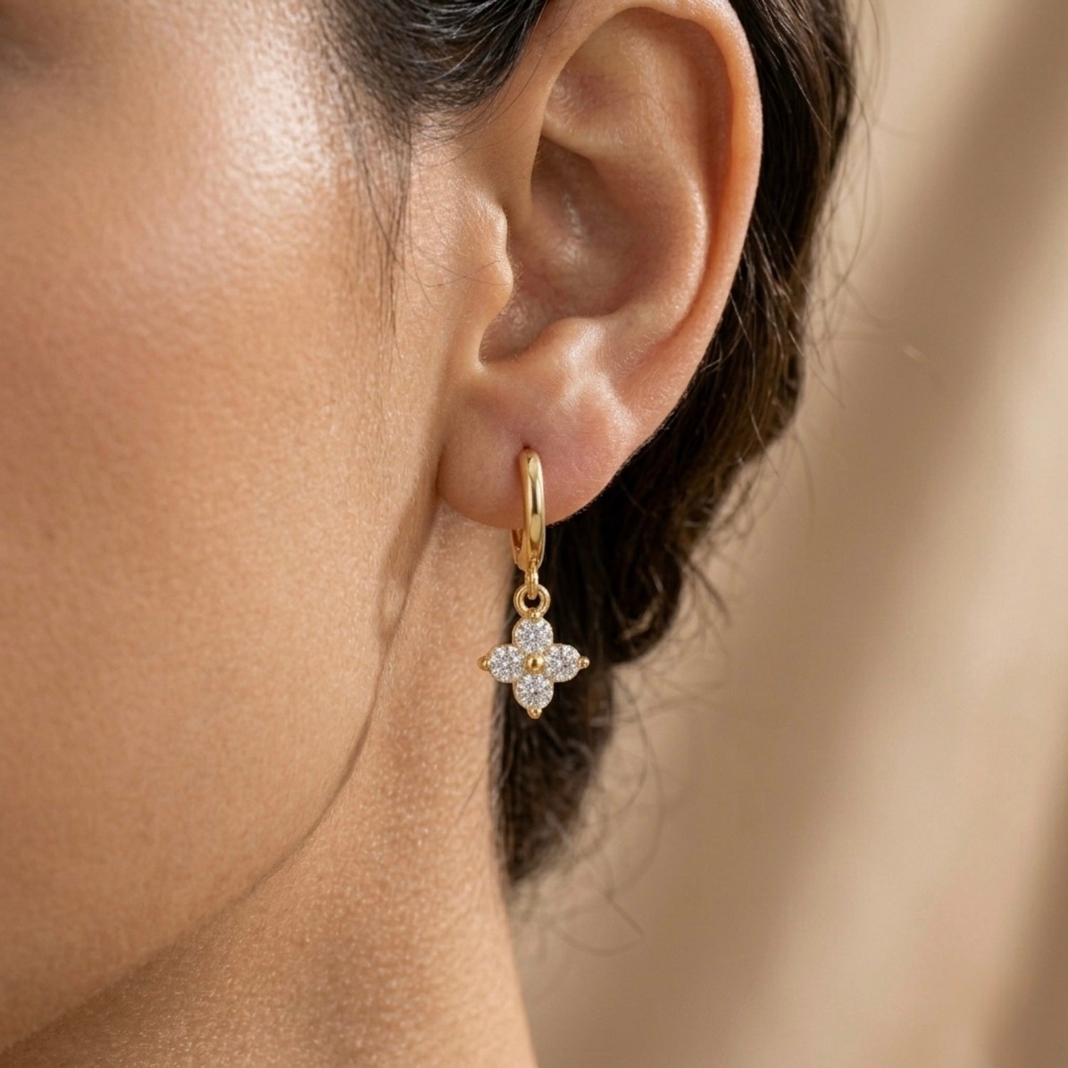 A gold-plated hoop earrings for women featuring a sparkling four-petal crystal clover drop, shown on a model