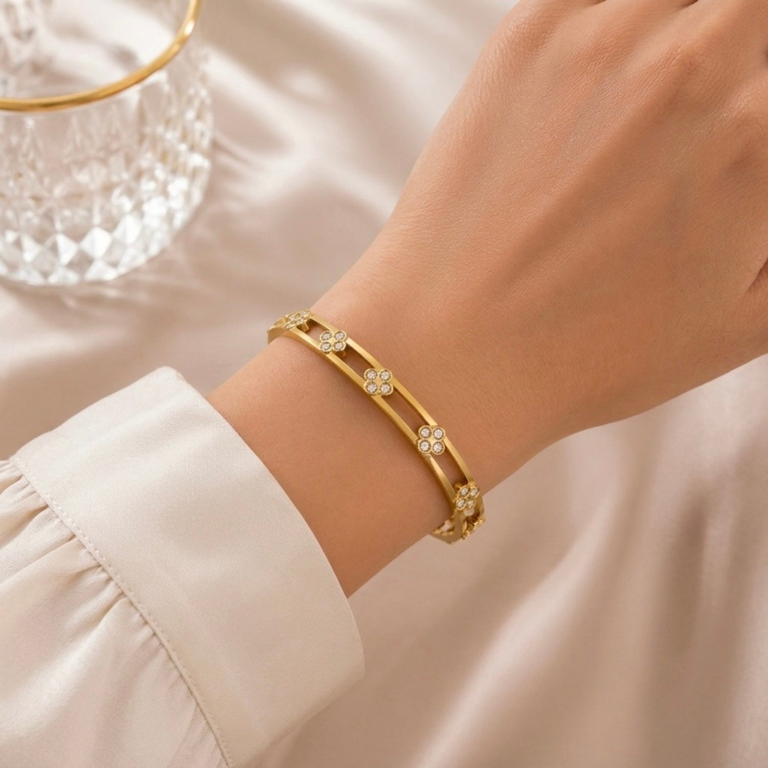 A gold-plated dual-band cuff bangle for women featuring four-petal clover crystal motifs and a secure side-hinge clasp, shown on a model