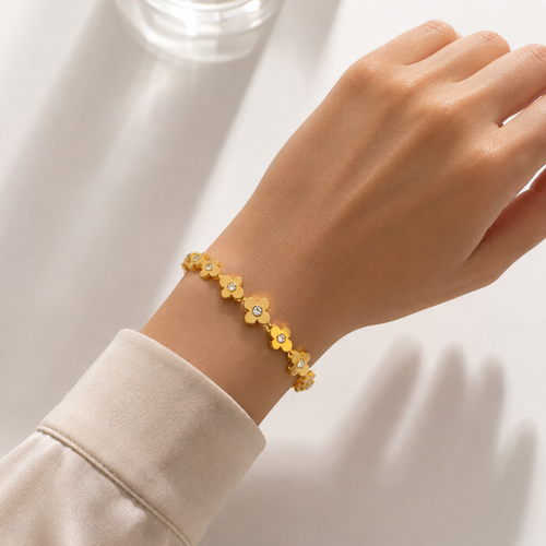 A gold-plated link bangle for women featuring a continuous row of clover motifs with crystal centers and a secure clasp, shown on a hand