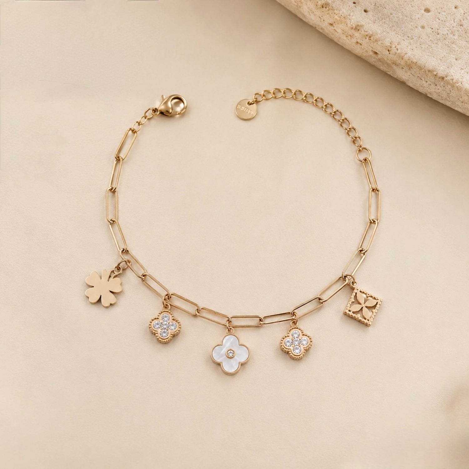 A close-view of a gold-plated chain bracelet for women featuring paperclip links and five floral and clover-themed charms with crystal and pearl accents.