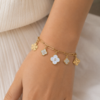 A gold-plated chain bracelet for women featuring paperclip links and five floral and clover-themed charms with crystal and pearl accents, shown on a model