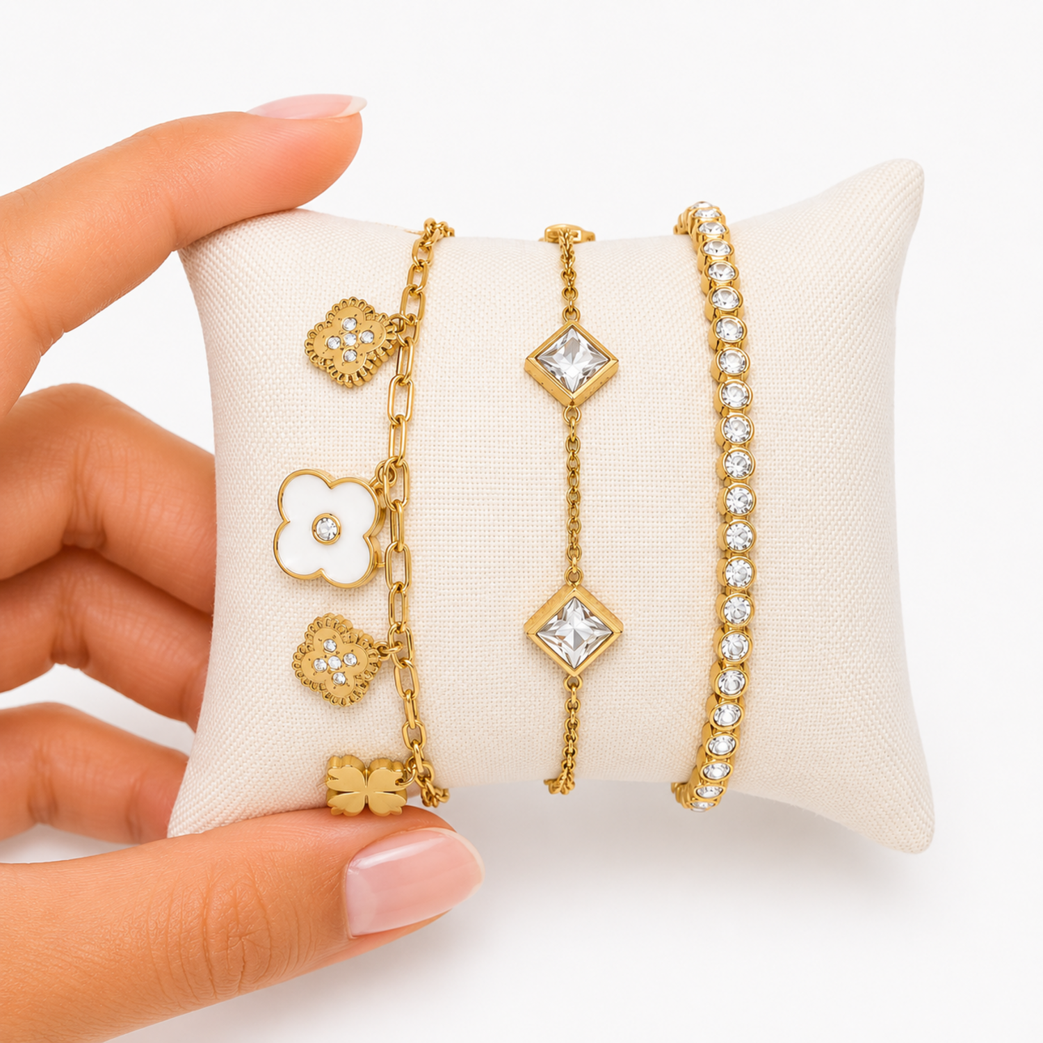 A close-view of a premium three-piece gold-plated bracelet stack for women featuring a white enamel clover paperclip chain, a five-crystal geometric station chain bracelet, and a continuous bezel-set crystal strand.