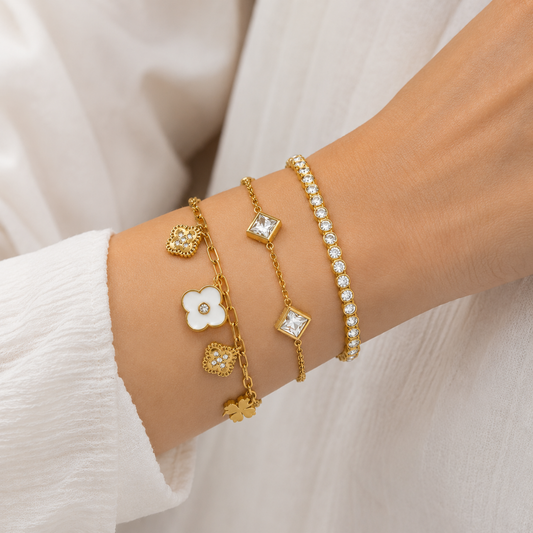 A premium three-piece gold-plated bracelet stack for women featuring a white enamel clover paperclip chain, a five-crystal geometric station chain bracelet, and a continuous bezel-set crystal strand, on a model
