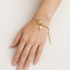 A gold-plated ladies bracelet featuring a gold paperclip chain on one side and a colorful beaded pearl strand with a shell charm on the other.