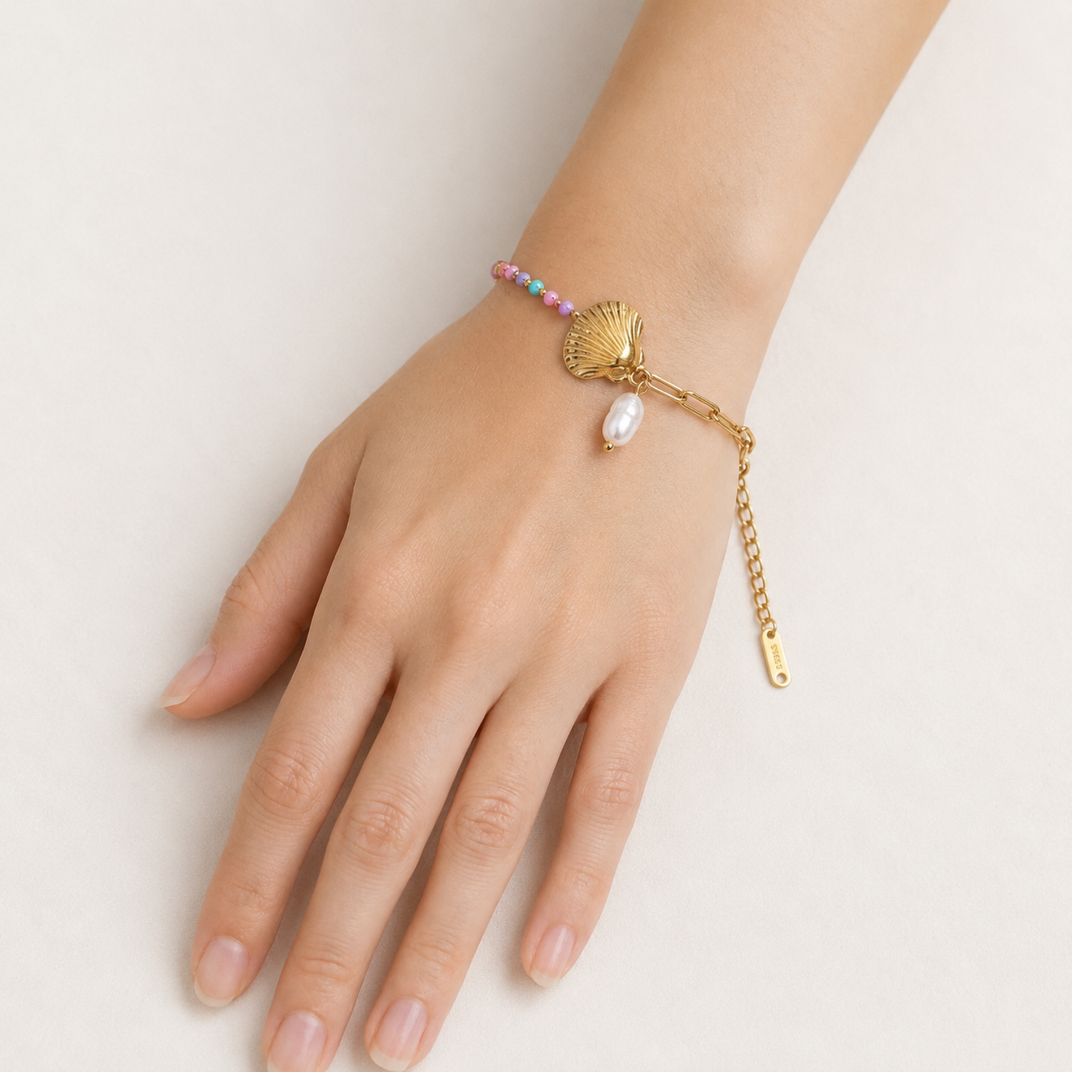 A gold-plated ladies bracelet featuring a gold paperclip chain on one side and a colorful beaded pearl strand with a shell charm on the other.