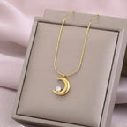 A gold-plated stainless steel chain for women featuring a polished crescent moon pendant set with a single sparkling clear crystal on display