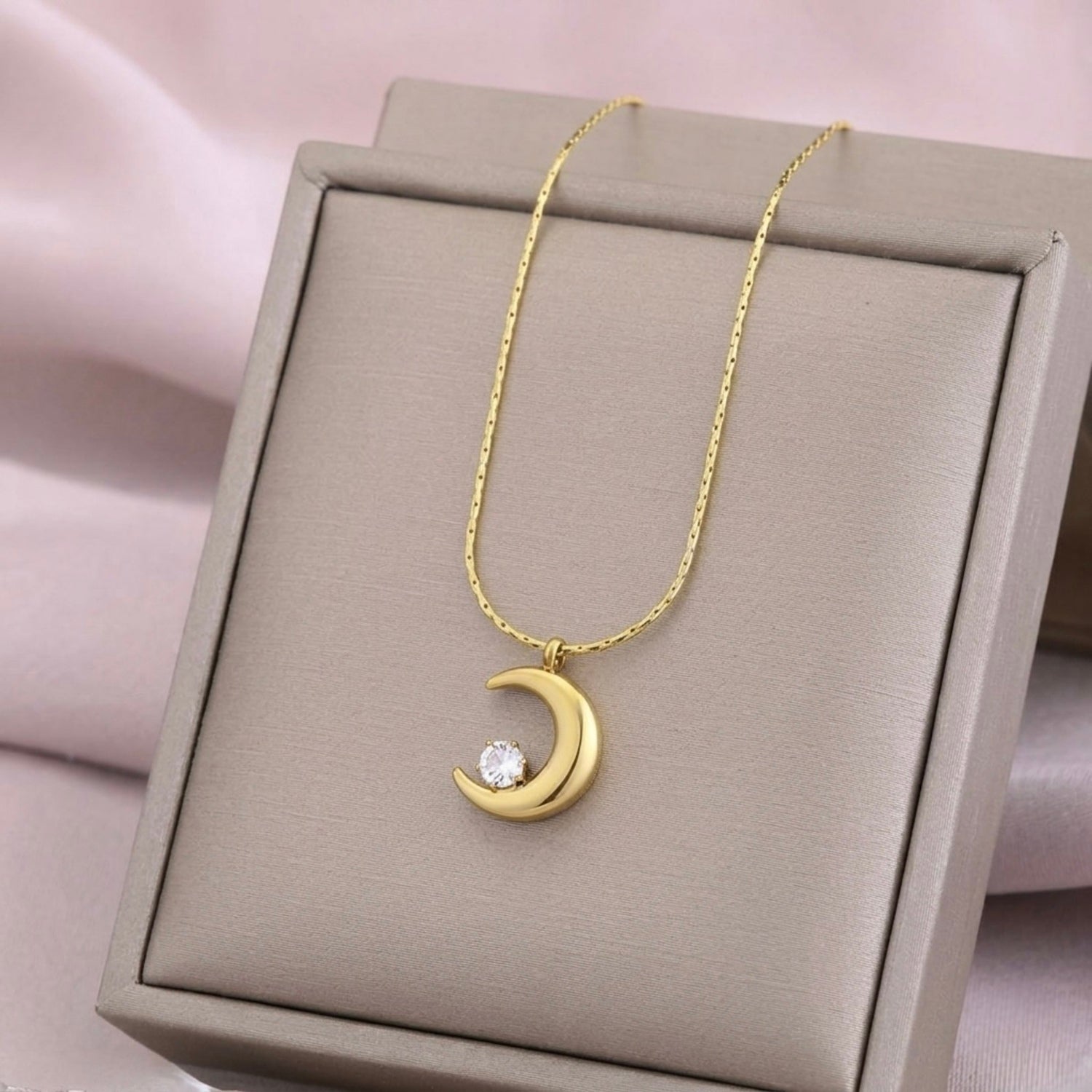 A gold-plated stainless steel chain for women featuring a polished crescent moon pendant set with a single sparkling clear crystal on display