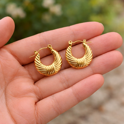 A pair of gold-plated textured croissant-style hoop earrings for women with a ribbed dome design, shown held in a hand.
