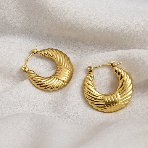 A pair of gold-plated textured croissant-style hoop earrings for women with a ribbed dome design, shown on a textured cream background