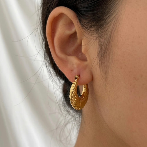 A gold-plated textured croissant-style hoop earrings for women with a ribbed dome design, shown on a model
