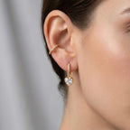 A gold-plated hoop earrings for women featuring a suspended heart-shaped clear crystal drop, shown on a model