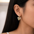 A gold-plated hoop earrings for women featuring a crystal bow drop with heart-shaped stones, shown on a model