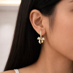 A gold-plated hoop earrings for women featuring a crystal bow drop with heart-shaped stones, shown on a model