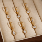 Gold earrings with clear stones on a beige jewelry display box