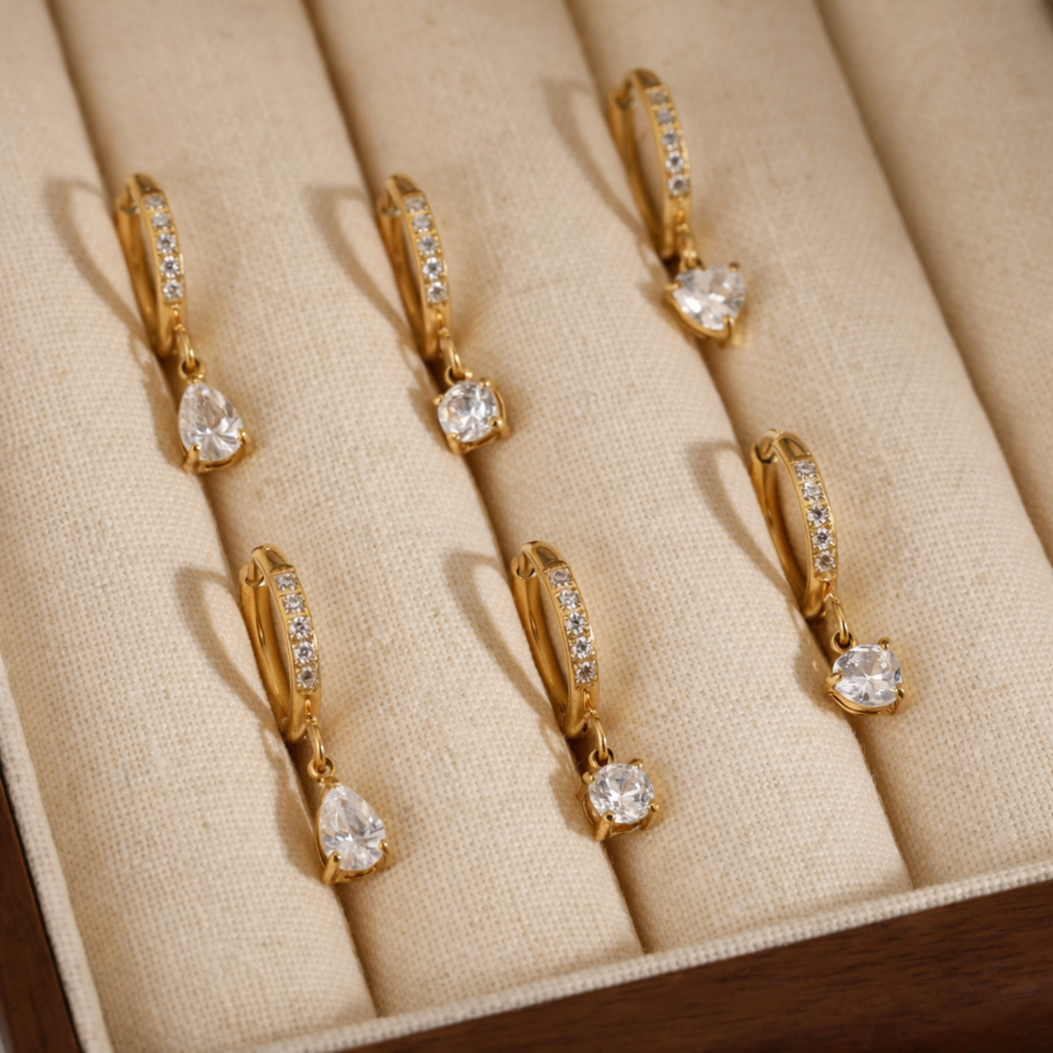 Gold earrings with clear stones on a beige jewelry display box