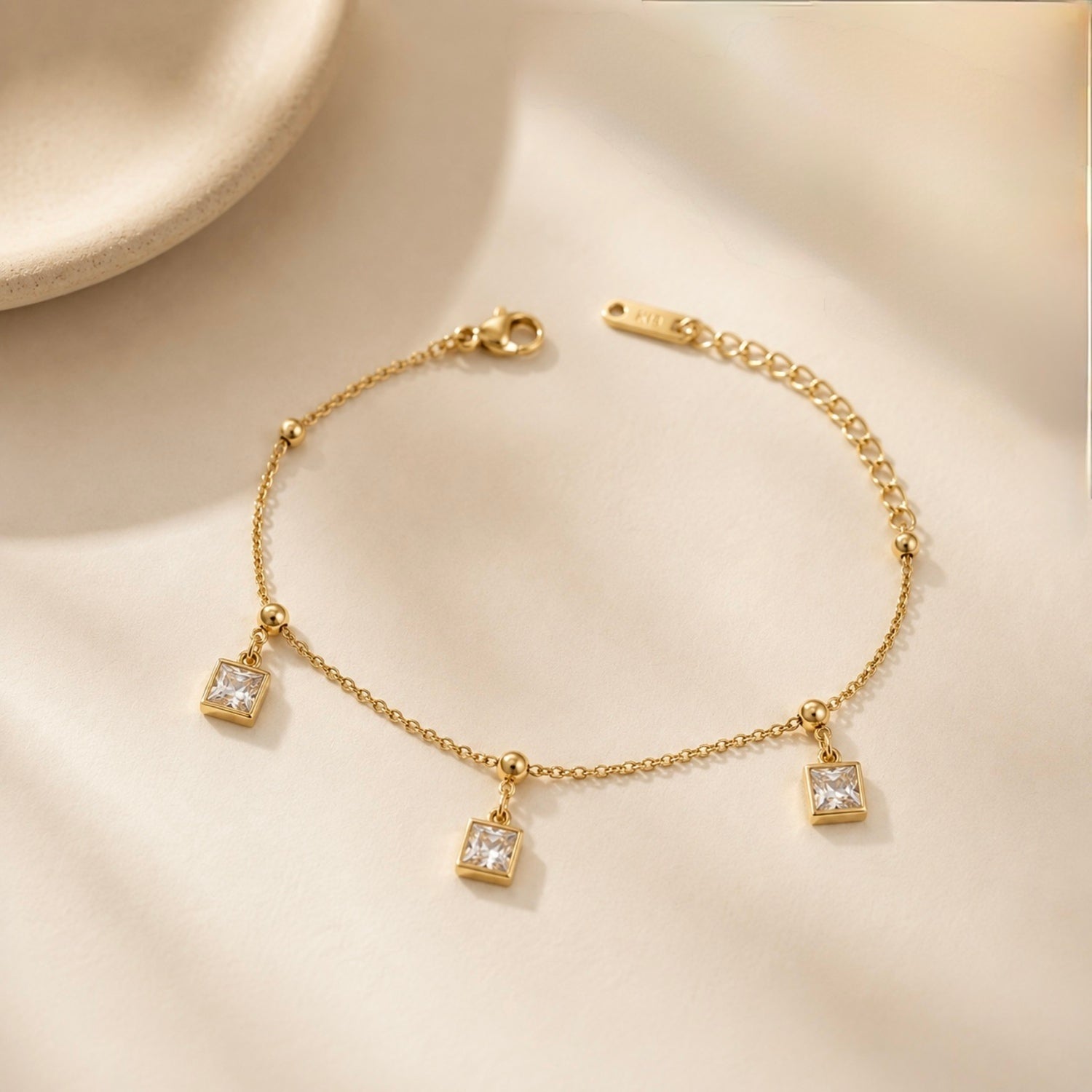 Gold bracelet with square charms on a beige background
