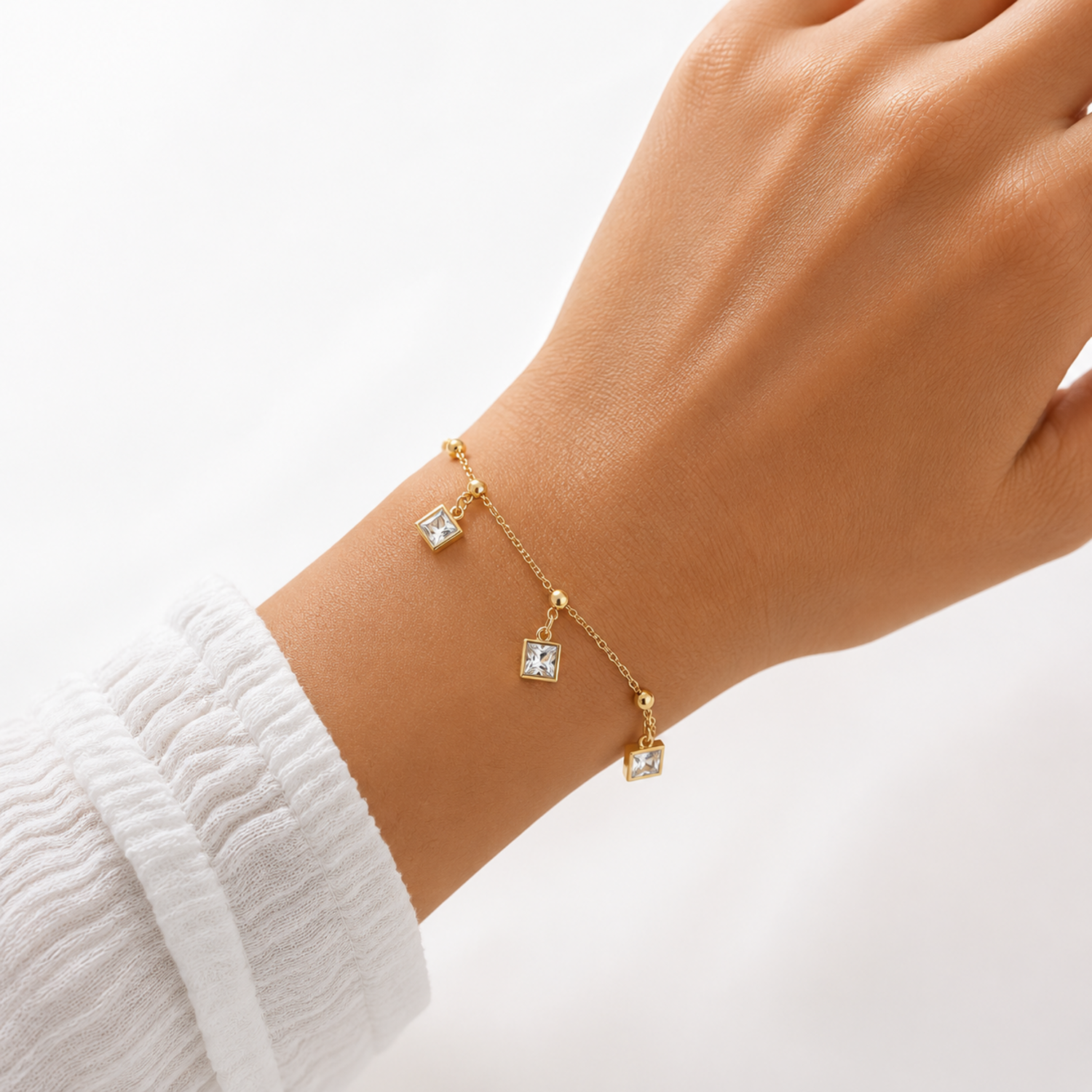 Gold bracelet with square-shaped charms on a wrist against a white background
